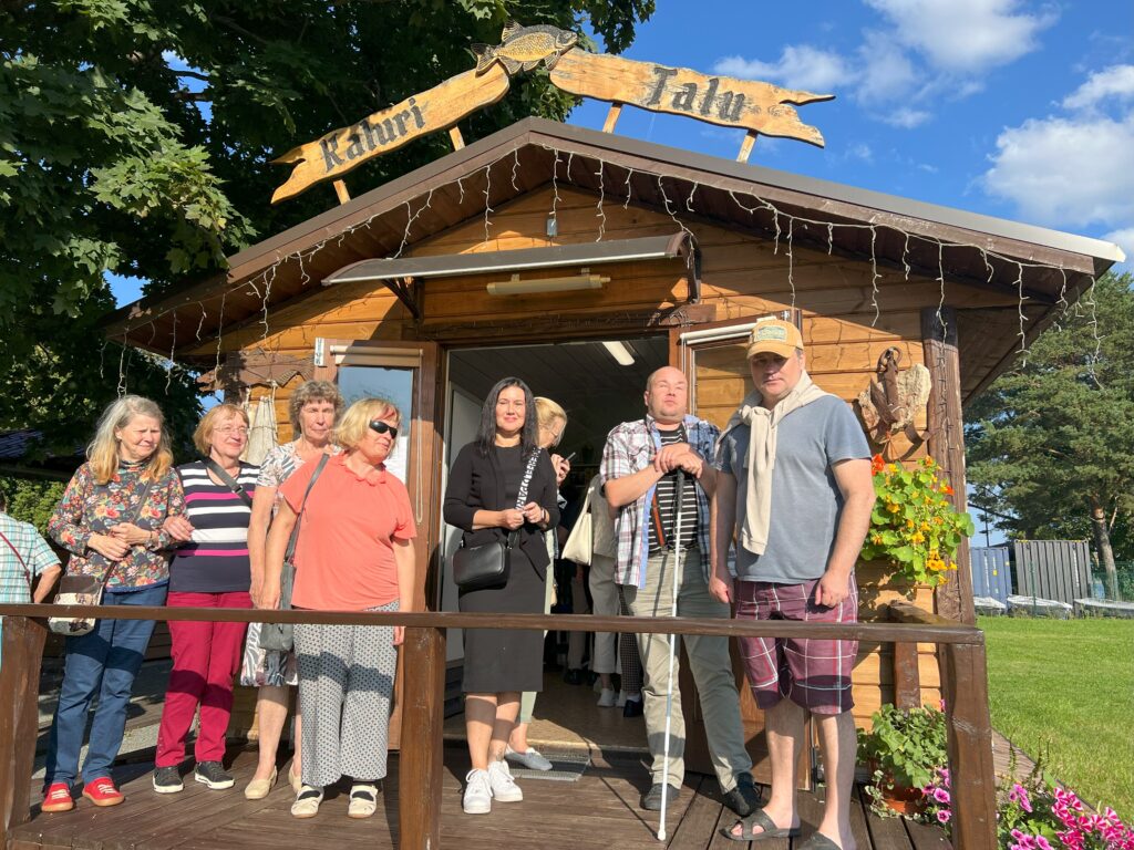 8 inimest seismas puidust hoone ees.